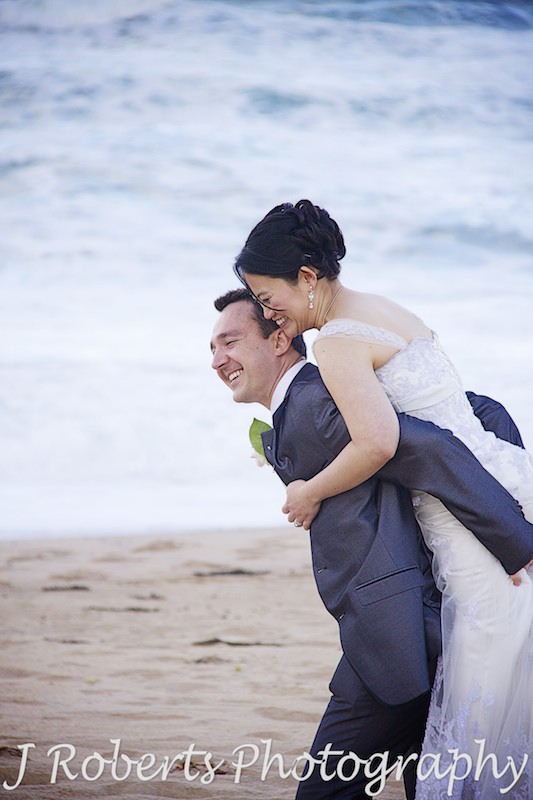 Groom piggy backing the bride at the beach - wedding photography sydney